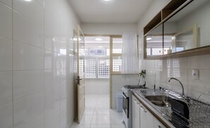 Una cocina moderna con azulejos blancos, electrodomésticos de acero inoxidable y un ventanal con vistas al exterior.