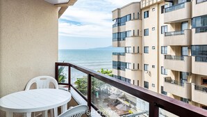 A balcony with a white table and chairs, overlooking a body of water and a building with multiple balconies. - Apt Foot in the Sand sea View in Meia Praia Evb308 (Itapema)