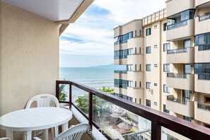 A balcony with a white table and chairs, overlooking a body of water and a building with multiple balconies. - Apt Foot in the Sand sea View in Meia Praia Evb308 (Itapema)