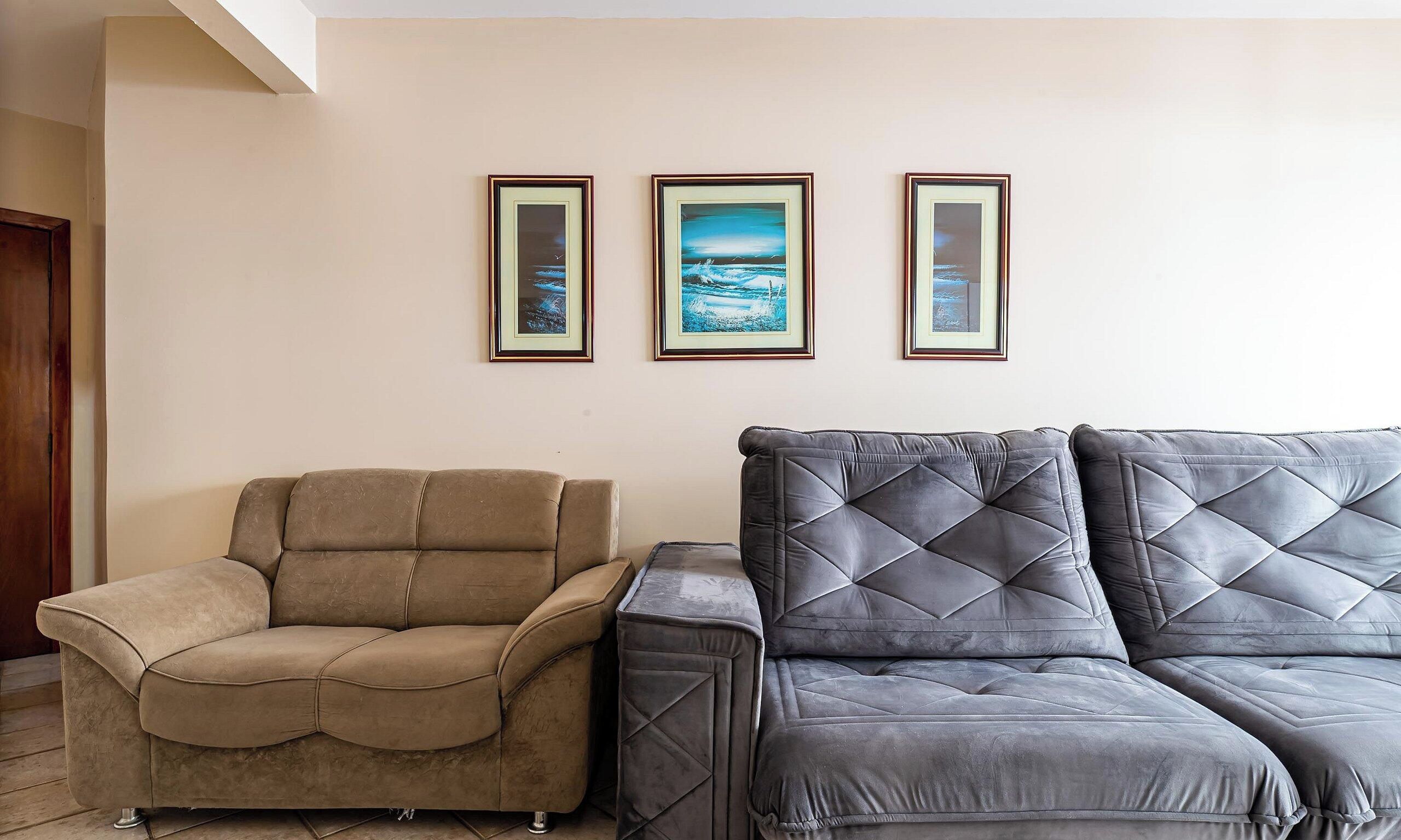 A living room with a beige sofa, a grey tufted sofa, and three framed artworks on the wall.