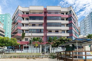 Un immeuble à plusieurs étages, doté de balcons, d’une entrée centrale et entouré de verdure.