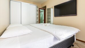 A neatly made bed with white linens, a wall-mounted TV, and a wardrobe with sliding doors. - Apt Foot in the Sand sea View in Meia Praia Evb308 (Itapema)
