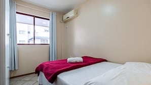 Ett hotellrum med en säng, ett fönster med gardiner, en luftkonditioneringsanläggning och ett klinkergolv.