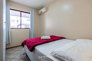 Une chambre d’hôtel avec un lit, une fenêtre avec des rideaux, un appareil de climatisation et un sol carrelé.