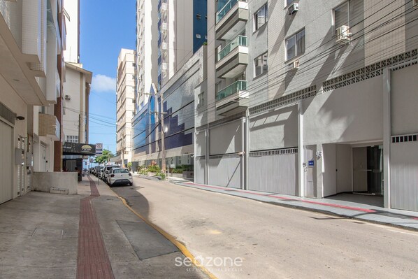 Une vue de rue d’un quartier résidentiel, avec des immeubles à plusieurs étages, un trottoir et des voitures garées.