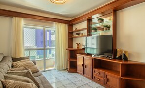 Un salon avec un canapé, un téléviseur, des étagères en bois et un balcon offrant une vue sur les immebles.