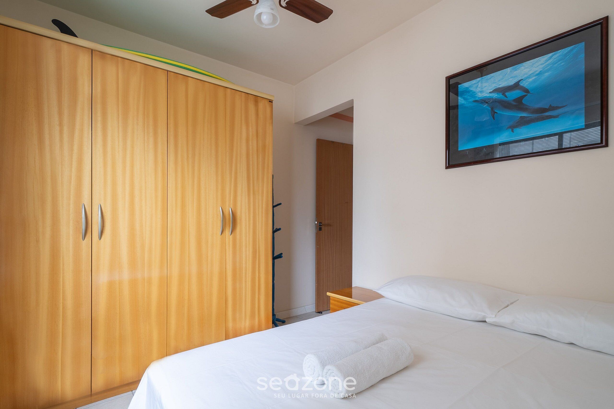 Ein Schlafzimmer mit einem Bett, einem Holzschrank und einem gerahmten Bild von Delfinen an der Wand.