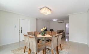Comedor con una mesa de vidrio rodeada de sillas acolchadas, una araña y un centro de mesa floral.
