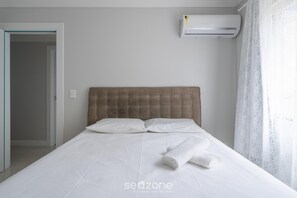 Una habitación de hotel con cama, cabecero, ventana con cortinas y equipo de aire acondicionado.