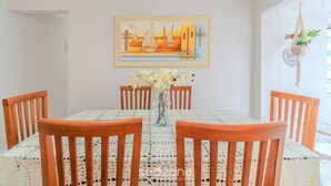 Un comedor con una mesa dispuesta para cuatro personas, sillas de madera, un mantel de encaje, un florero con flores y un cuadro en la pared.