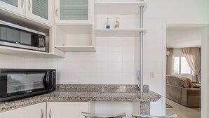 Una cocina con encimera de granito, microondas negro y pileta doble. Hay dos taburetes de bar y una ventana con cortinas.