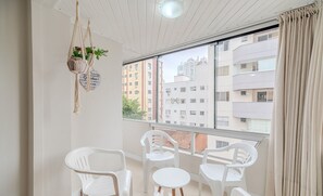 A balcony with white plastic chairs and a small round table, a macrame plant hanger, and a view of multi-story buildings. - 3 Bedroom apt 300m fr the Central Beach BC Idn0402 (Balneário Camboriú)