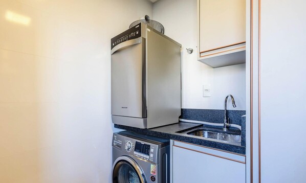 A compact kitchen with a washing machine, a built-in microwave, and a sink. - Modern and Fully Equipped Apartments Just Minutes From the sea at Meia Praia - GRI (Itapema)