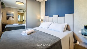 A hotel room with a large bed, a bedside table, a mirror, and a blue accent wall. - Modern and Fully Equipped Apartments Just Minutes From the sea at Meia Praia - GRI (Itapema)