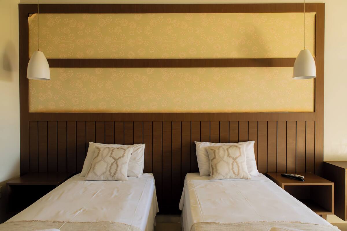 Habitación de hotel con dos camas, cabecera de madera y dos lámparas colgantes.