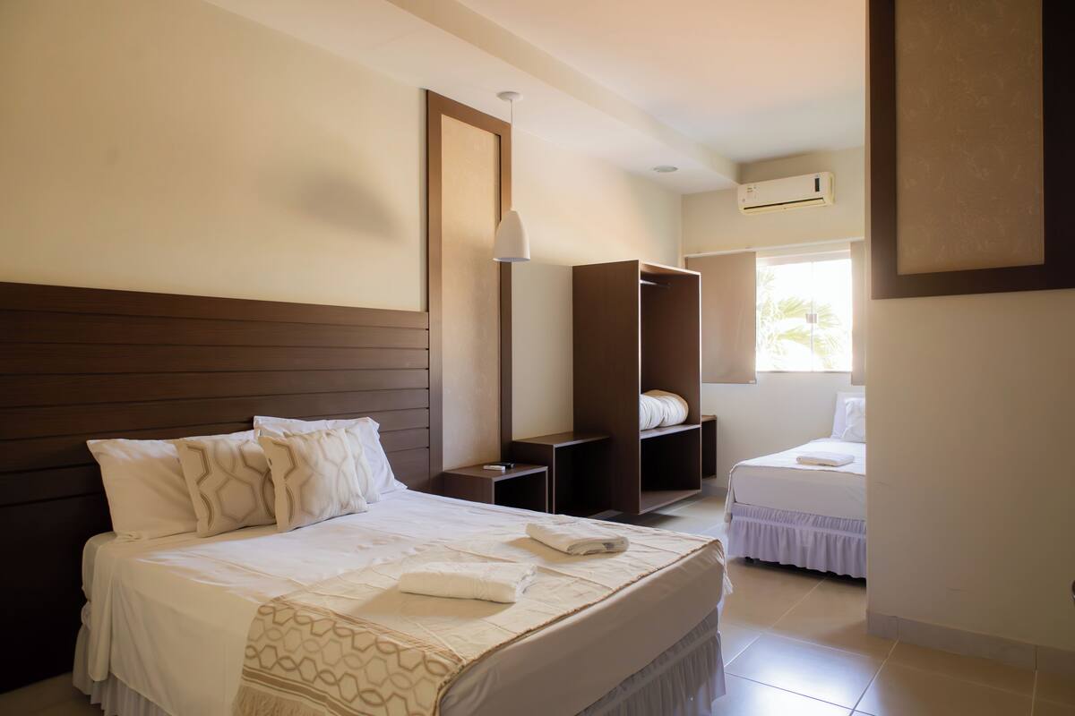 Una habitación de hotel con una cama grande, un armario, una mesita de noche y una ventana con vistas.
