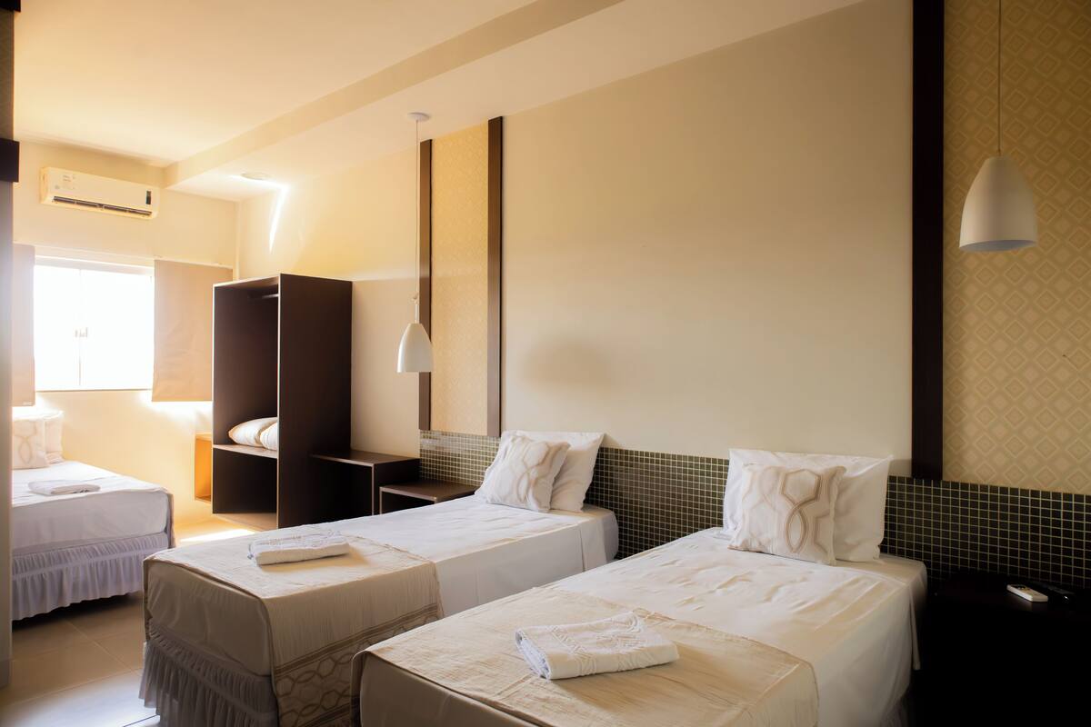 Una habitación de hotel con dos camas individuales, un armario, una mesita de noche y una lámpara colgante.