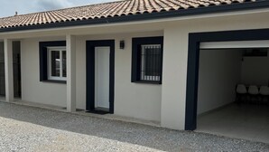 A building with a tiled roof, a gravel driveway, and a covered parking area. - New house ground floor 2 bedrooms garage terrace (La Tour-du-Crieu)