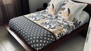 A neatly made bed with patterned bedding, a bedside table with a lamp, and a window with curtains. - New house ground floor 2 bedrooms garage terrace (La Tour-du-Crieu)