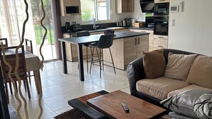 A modern kitchen with a central island, a dining area with chairs, a sofa, and a coffee table. - New house ground floor 2 bedrooms garage terrace (La Tour-du-Crieu)