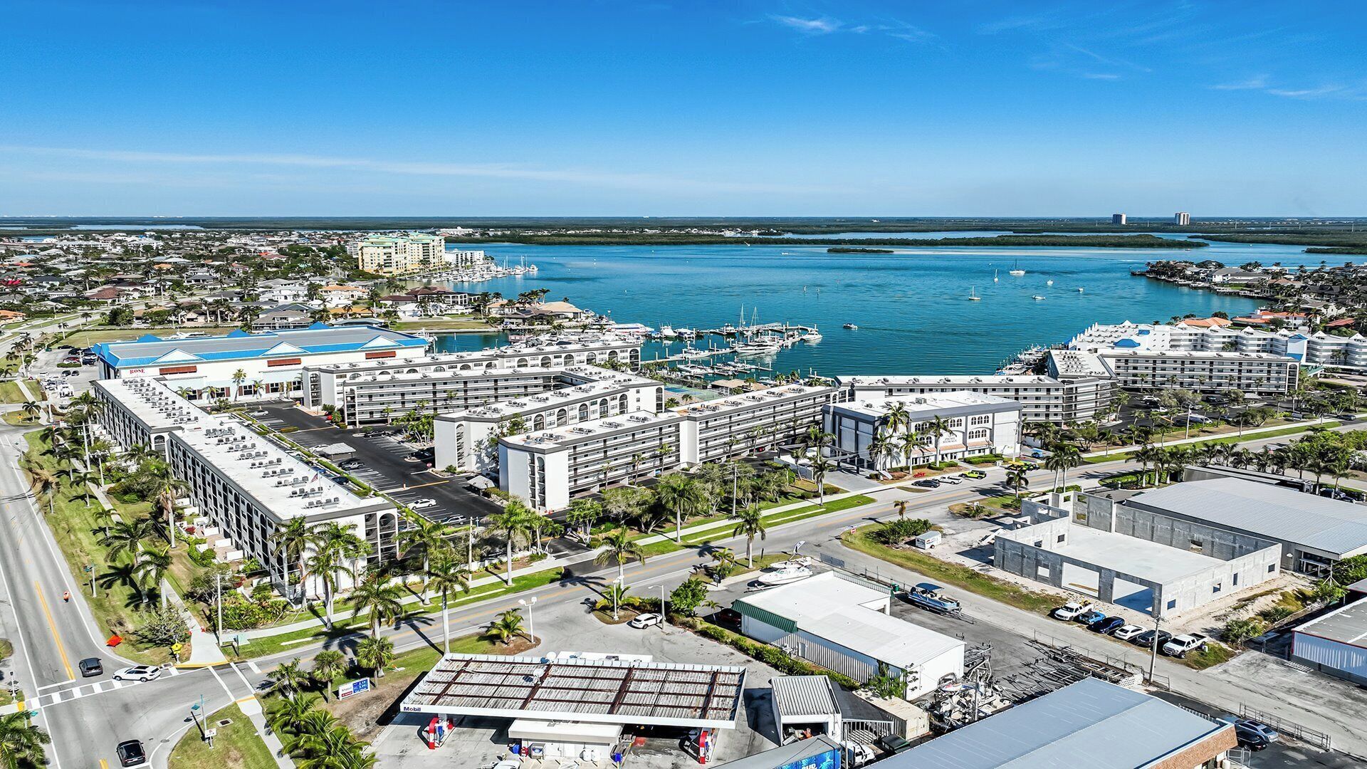 Un paisaje urbano costero con un puerto deportivo, hoteles y un cielo azul despejado.