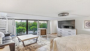 A modern bedroom with a bed, a TV, a desk, and a staircase leading to an outdoor area. - Three-bedroom, two-bath condo at Anglers Cove. Partial view of water and pool. (Marco Island)