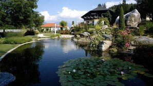 A hotel with a garden pond, surrounded by lush greenery and a large rock. - Seehotel Steiner (Seeboden)