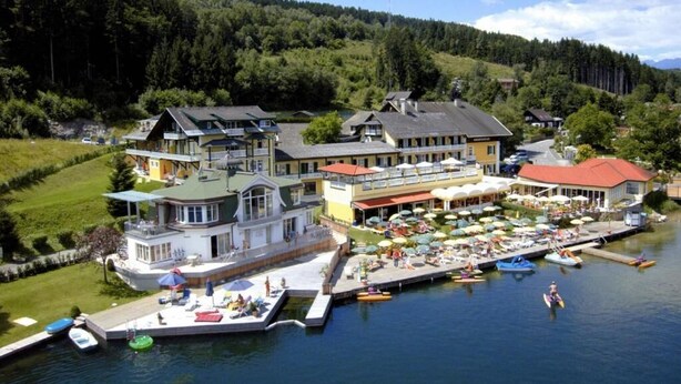 A lakeside hotel with multiple buildings, a dock with boats, and a marina with umbrellas. - Seehotel Steiner (Seeboden)