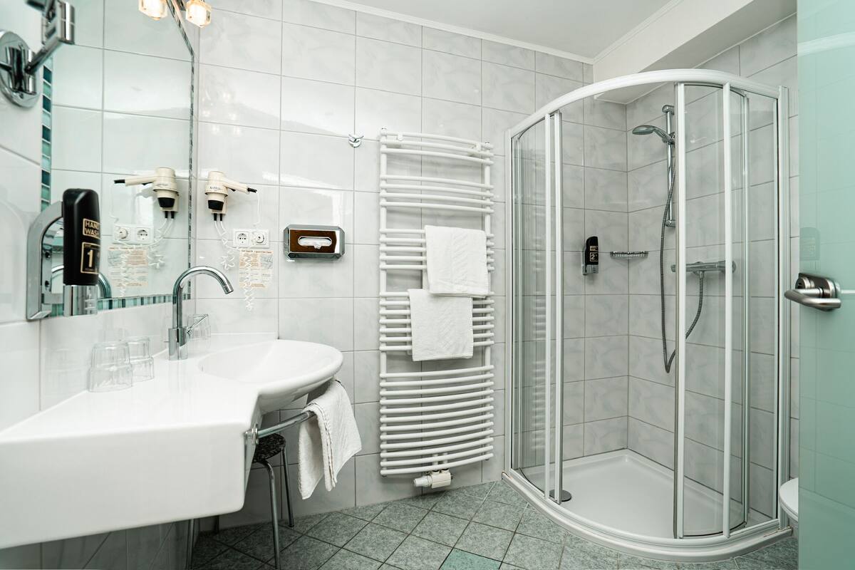 A modern bathroom with a glass-enclosed shower, a white sink with a mirror, and a towel rack.