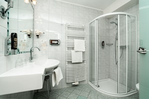 Ein modernes Badezimmer mit einer gläsernen Duschkabine, einem weißen Waschbecken mit Spiegel und einem Handtuchhalter.