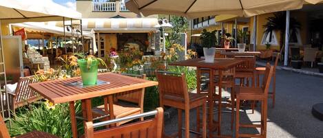 Un espace extérieur aménagé avec des tables et des chaises en bois, entouré de plantes en pot et agrémenté de parasols.