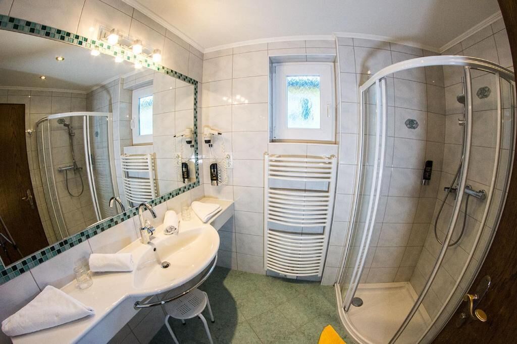 A bathroom with a sink, mirror, towel rack, shower, and a window.