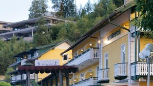A hotel with a stone pathway leading to a wooden pergola, surrounded by well-maintained bushes and a fire feature in the foreground. - Seehotel Steiner (Seeboden)