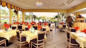 A restaurant with multiple tables set for dining, featuring yellow tablecloths and patterned chairs. - Seehotel Steiner (Seeboden)