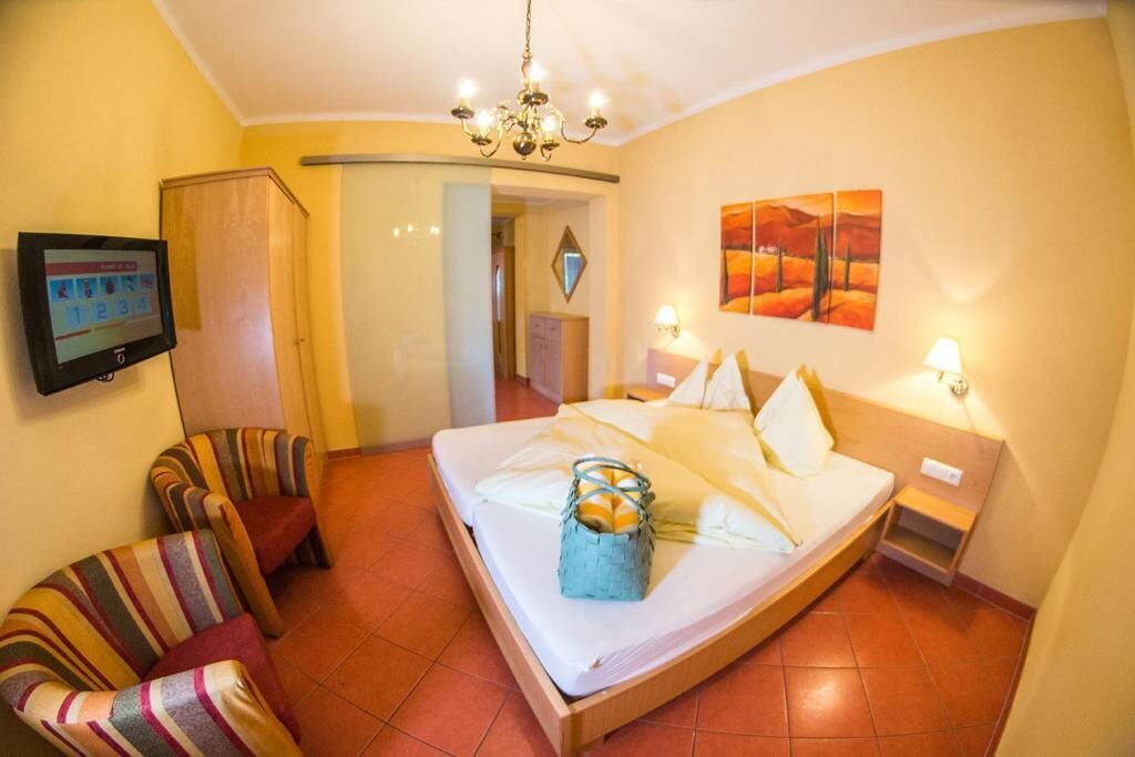 Una habitación de hotel con cama, sillones a rayas, televisor, un cuadro y una araña.