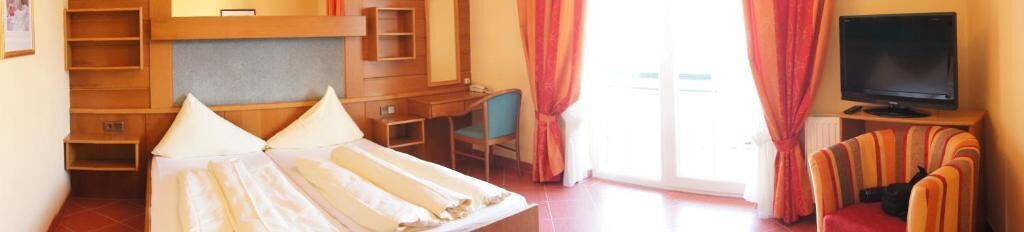 A hotel room with a bed, a desk, a chair, a television, and a window with curtains.