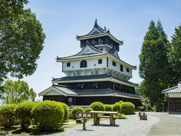 Ett traditionellt japanskt slott med flera våningar och ett framträdande centralt torn, omgivet av välskött grönska och en grusgång.