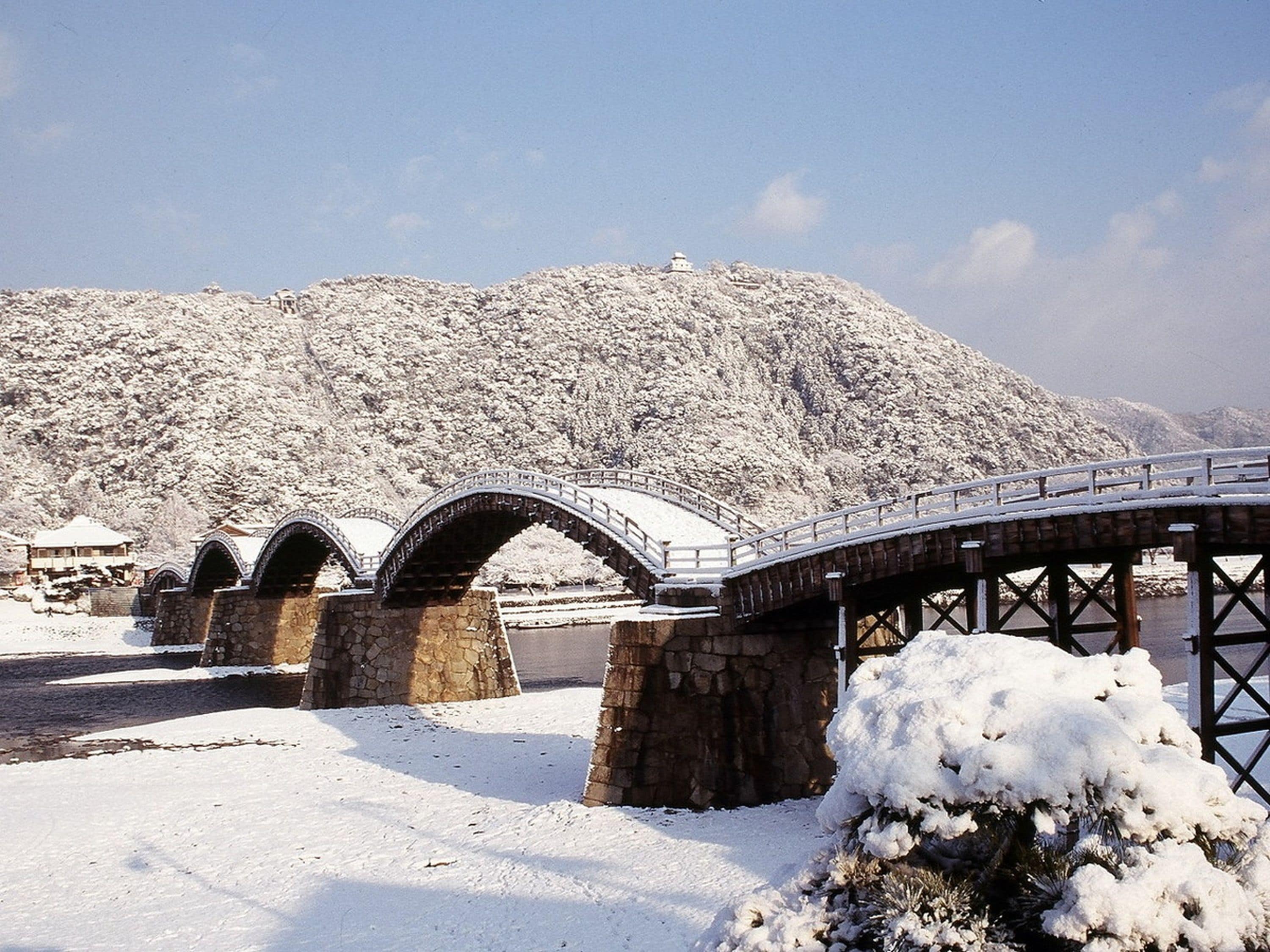 A stone bridge with multiple arches over a snow-covered landscape, leading to a building with a snow-covered roof.