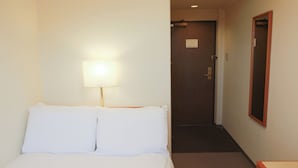 Una habitación de hotel con una cama, una mesita de noche, una lámpara, una puerta y un espejo.