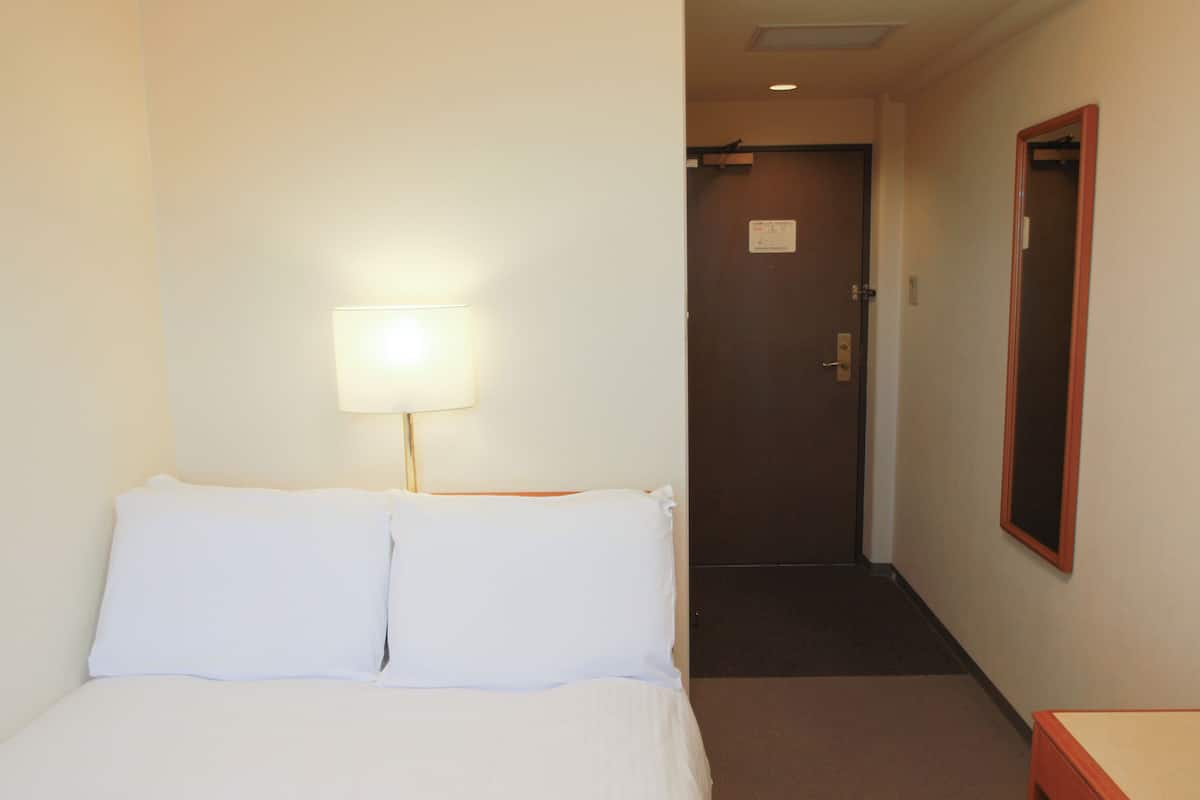 A hotel room with a bed, a nightstand, a lamp, a door, and a mirror.