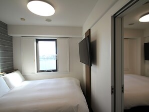 Quarto de hotel com duas camas, televisão de tela plana na parede, janela com persianas e luminária no teto.