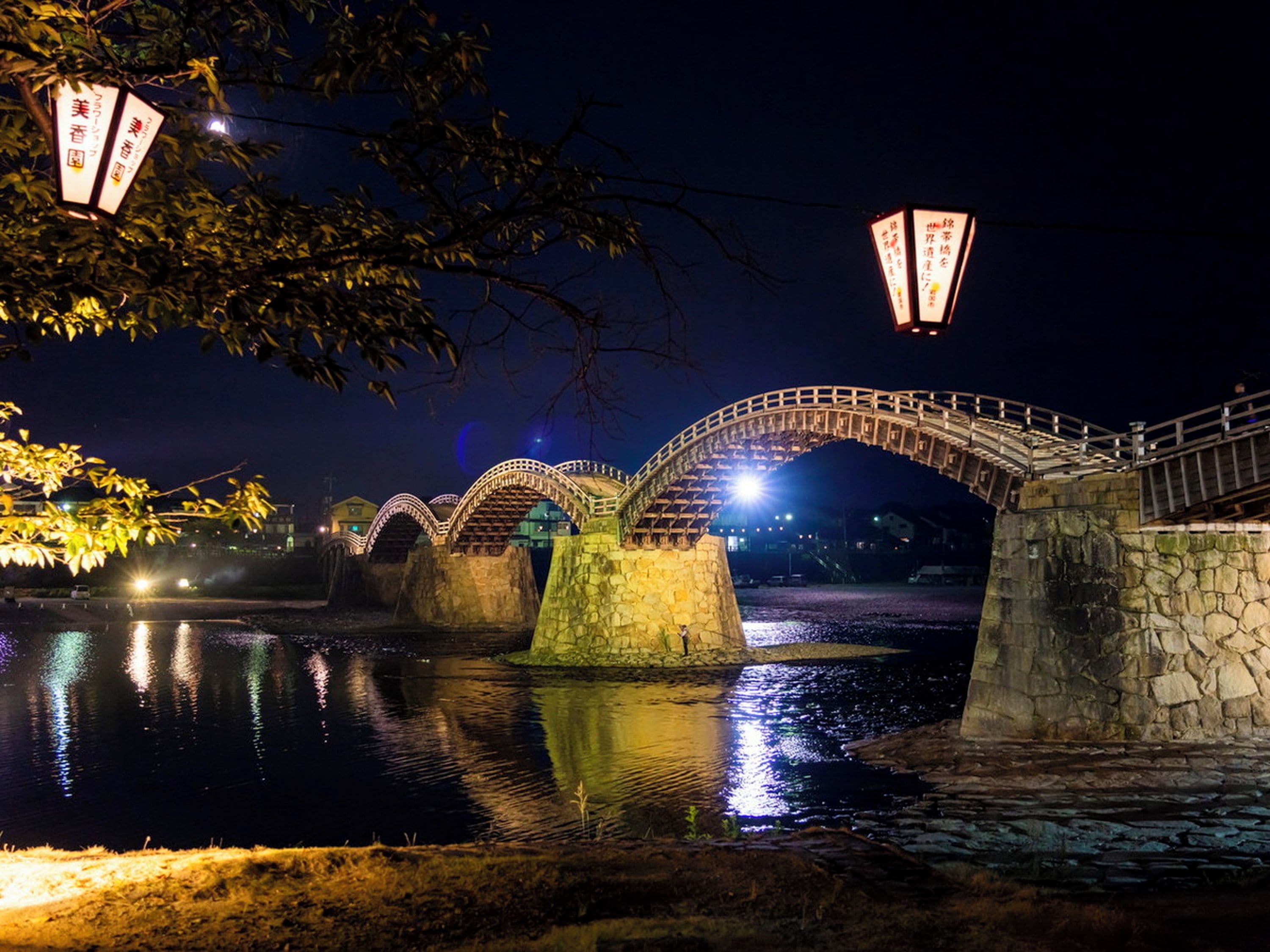 Eine Steinsche Brücke über Wasser bei Nacht mit beleuchteten Schildern.