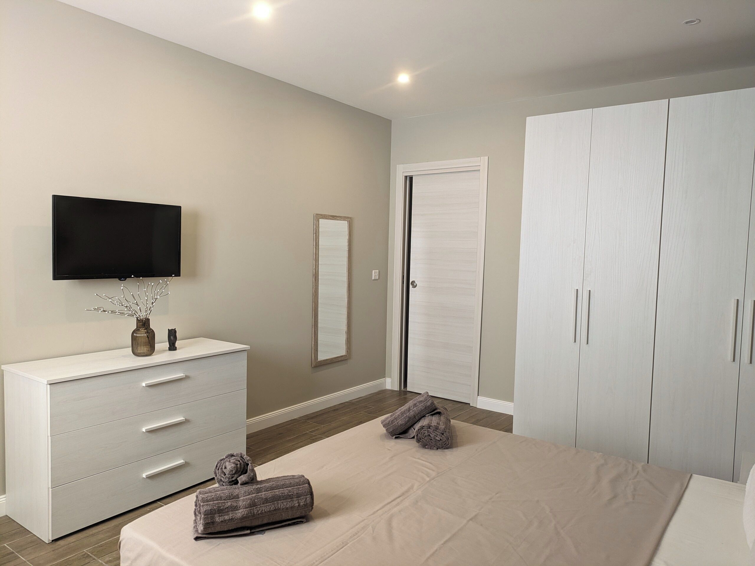 A bedroom with a bed, a dresser, a TV, a mirror, and a wardrobe.