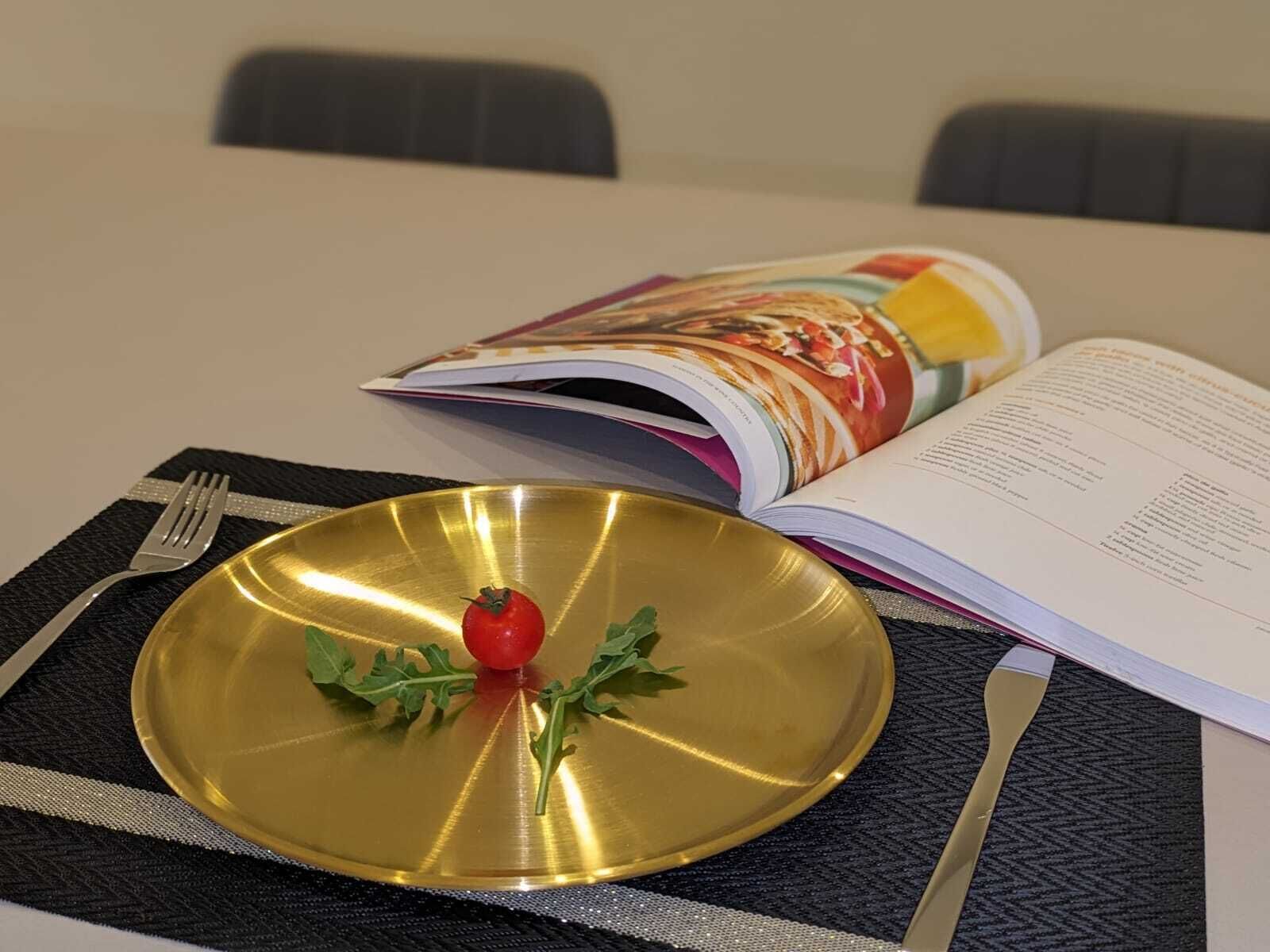 A table with a gold plate, a fork, a knife, and an open magazine.