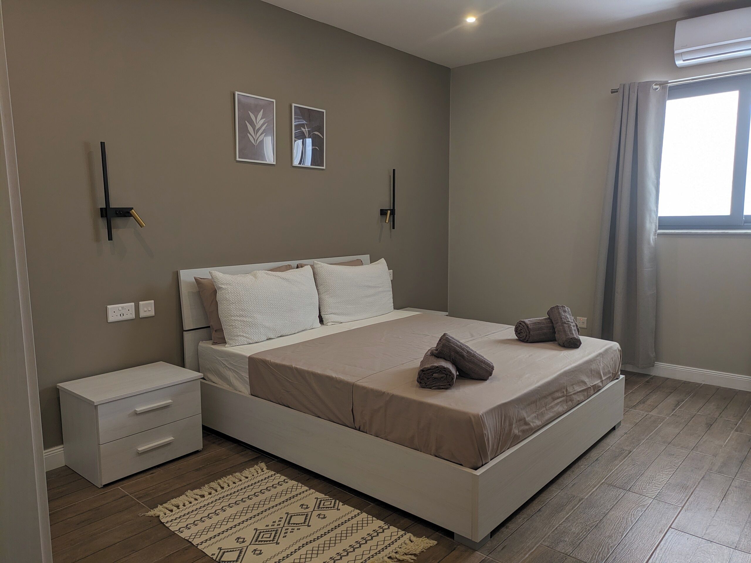 Ein modernes Schlafzimmer mit einem großen Bett, einem Nachttisch, einer Wandlampe und einem Fenster mit Vorhängen.