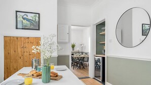 A modern kitchen with a white countertop, a wooden door, and a dining area with a table set for two. - Palm House (Newquay)