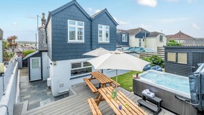 A residential property with a deck, a hot tub, and a patio area with wooden benches and an umbrella. - Palm House (Newquay)