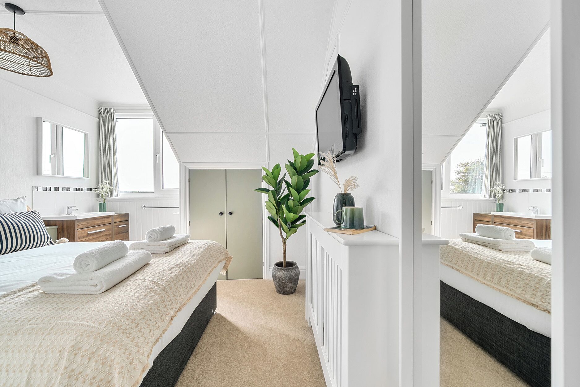 A modern bedroom with a large bed, a TV mounted on the wall, and a potted plant.