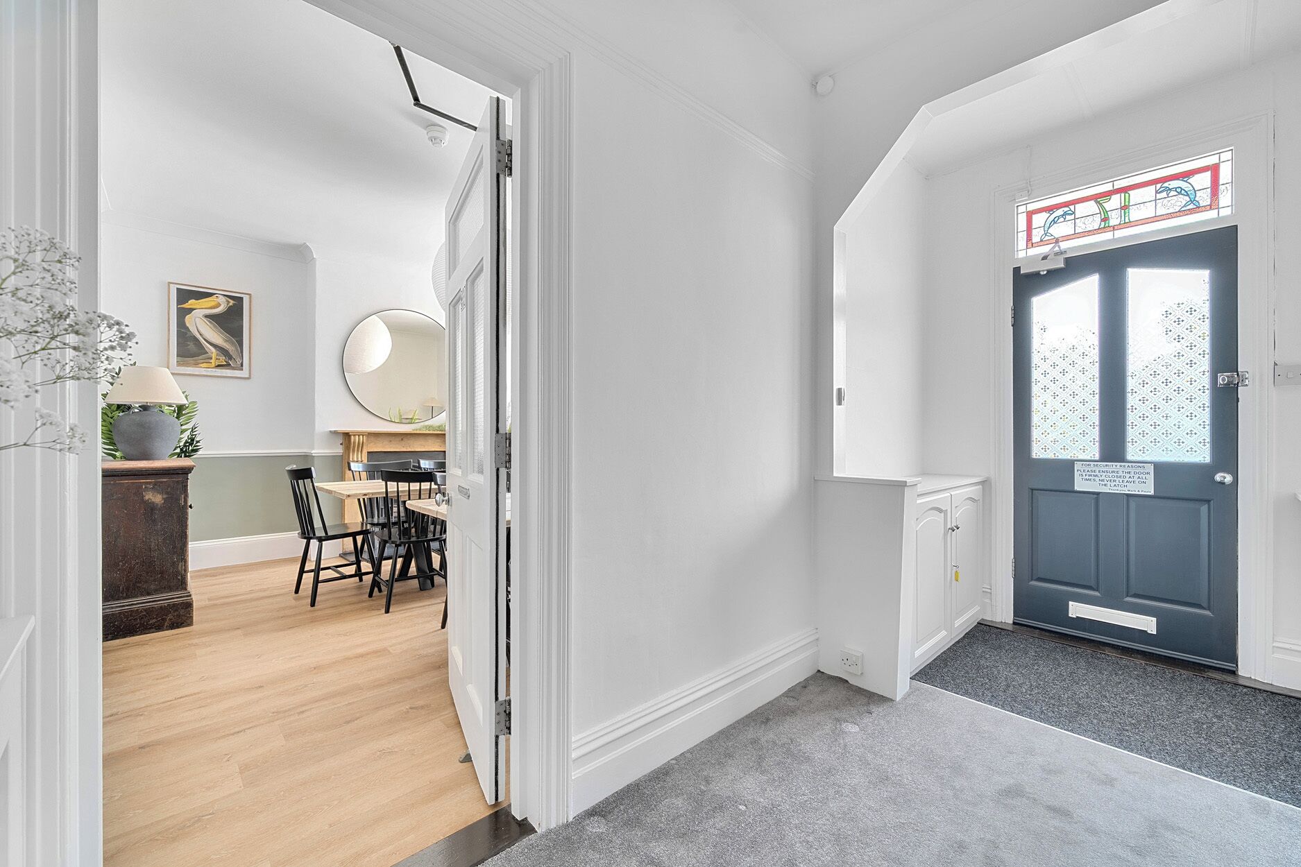 A hallway with a dining area, a dark blue door with a security notice, and a white wall with a framed picture.