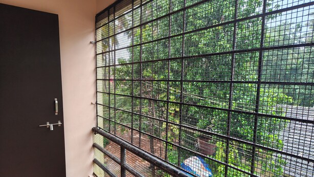 Una habitación con una ventana protegida por una celosía metálica, una puerta con manija y vistas al exterior con vegetación.